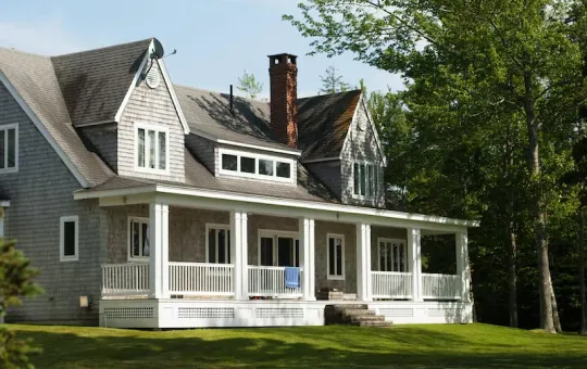Custom farmhouse home with wrap-around porch, cedar shingle siding, dormers, and brick chimney built by Design First Builders