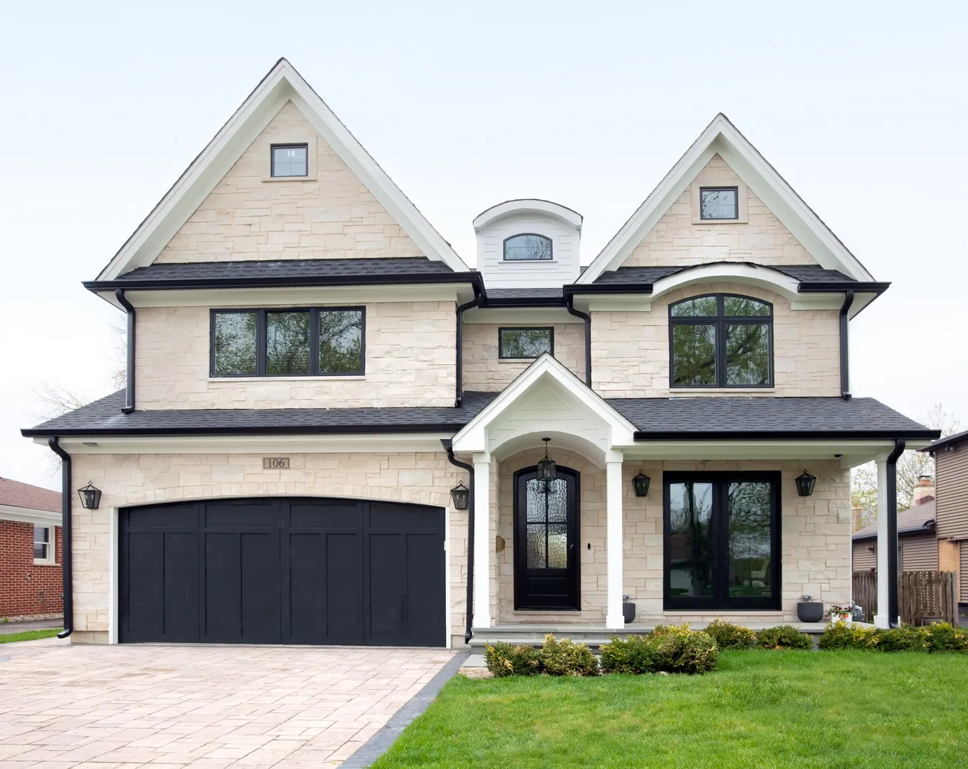 Custom luxury home built by Design First Builders featuring natural stone exterior, black window trim, arched front door, and professional landscaping in Chicago