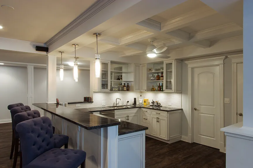 Luxury basement kitchenette renovation by Design First Builders featuring coffered ceiling, gray cabinets, black granite countertops, pendant lighting, and wet bar in Burr Ridge Illinois