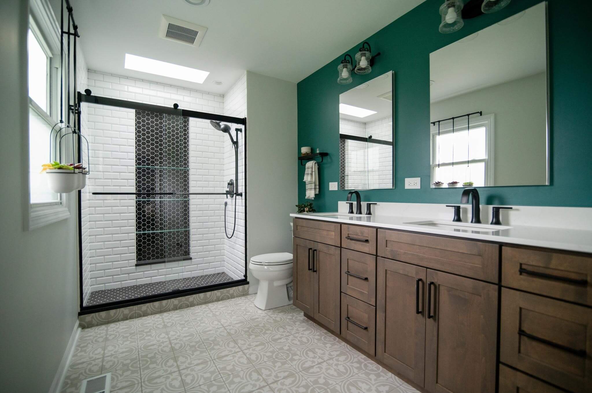 Design First Builders bathroom renovation with bold green accent wall, black hexagon tile shower, wood vanity, and patterned floor tiles