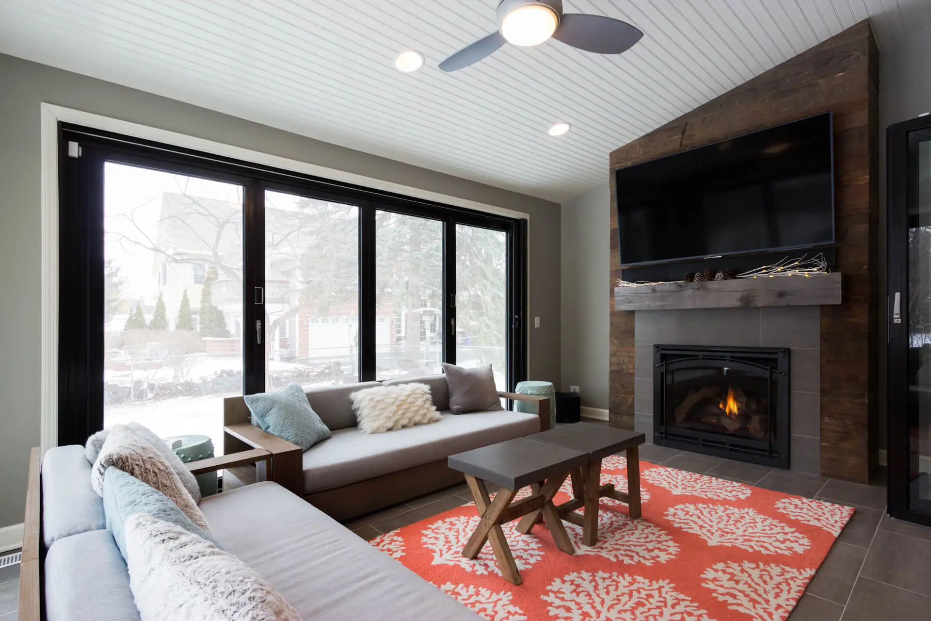 Modern home addition by Design First Builders featuring sunroom with black window frames, beadboard ceiling, stone fireplace, and patio doors in Glen Ellyn, Illinois