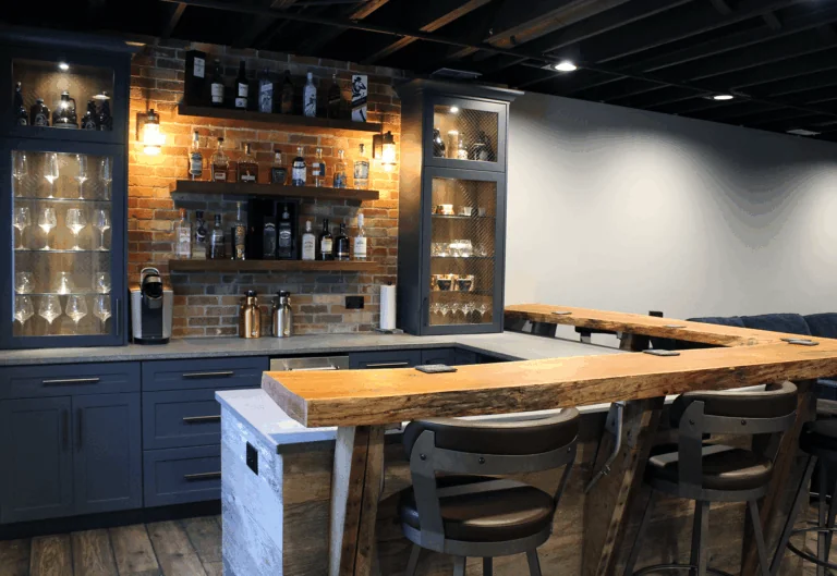 Design First Builders Lombard basement renovation featuring custom bar with live-edge wood countertop, exposed brick wall, navy cabinets, and glass display shelving