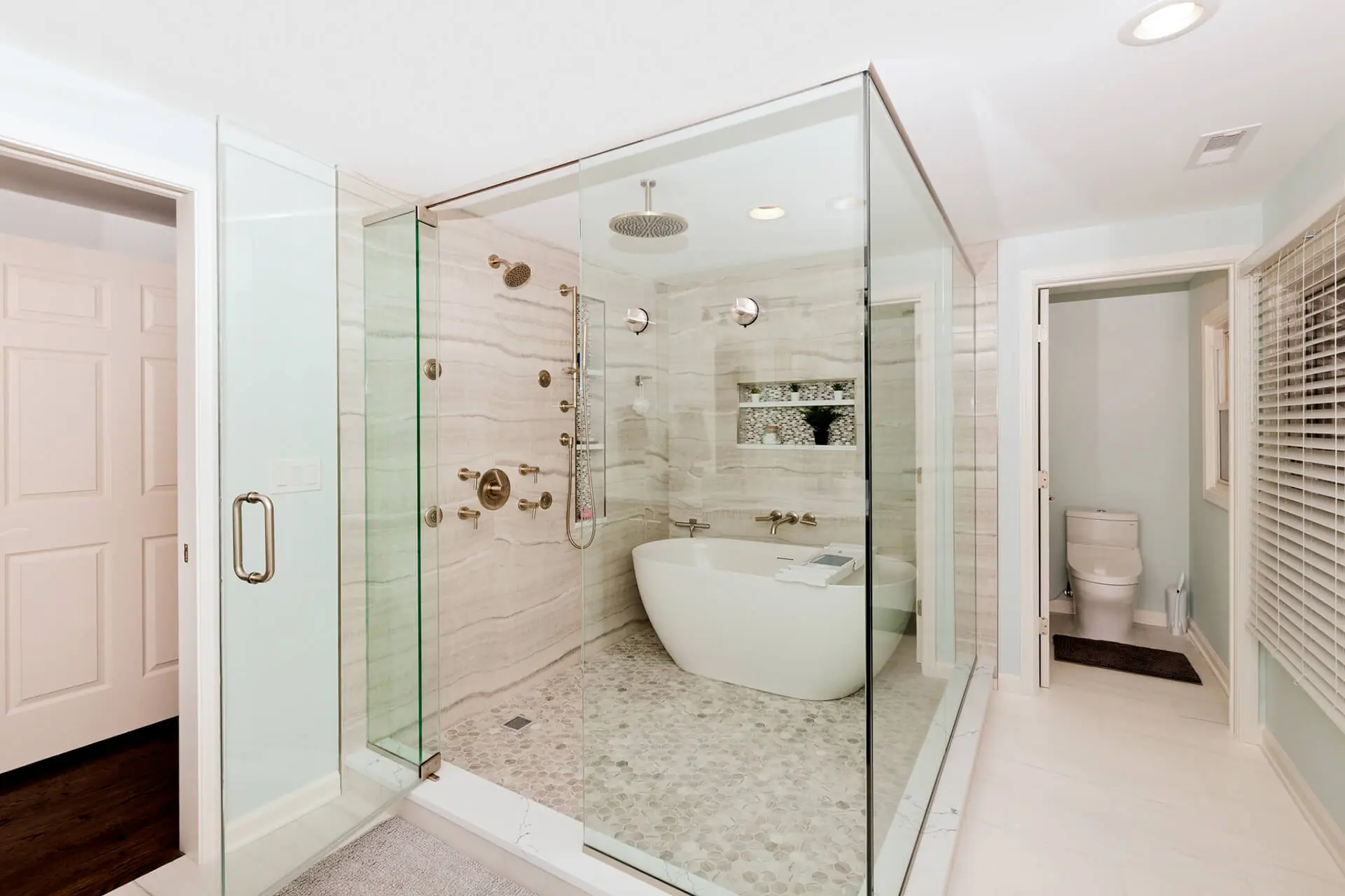 Design First Builders Naperville luxury master bathroom with glass-enclosed shower, freestanding soaking tub, marble walls, and brass fixtures