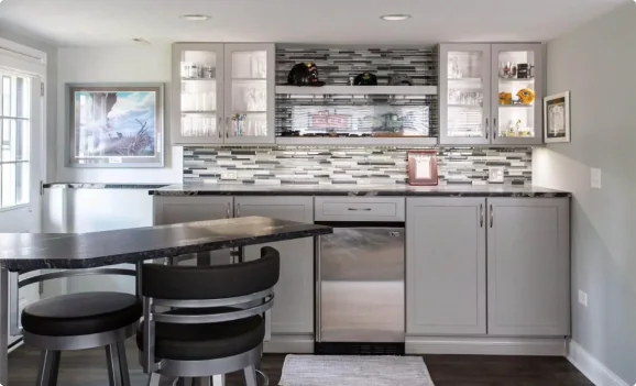 Modern kitchen renovation by Design First Builders featuring gray flat-panel cabinets, mosaic tile backsplash, black quartz countertops, stainless steel appliances, and breakfast bar in Illinois