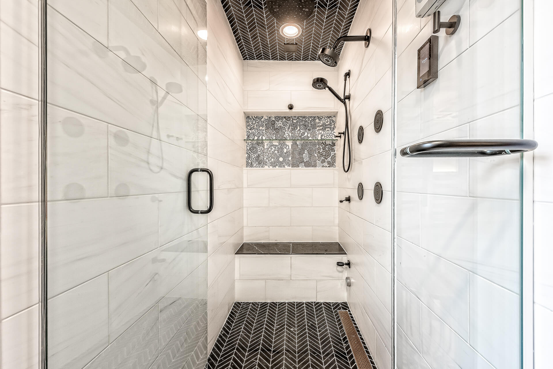 Design First Builders Park Ridge luxury shower with black chevron tile ceiling and floor, white marble walls, multiple body sprays, and built-in bench