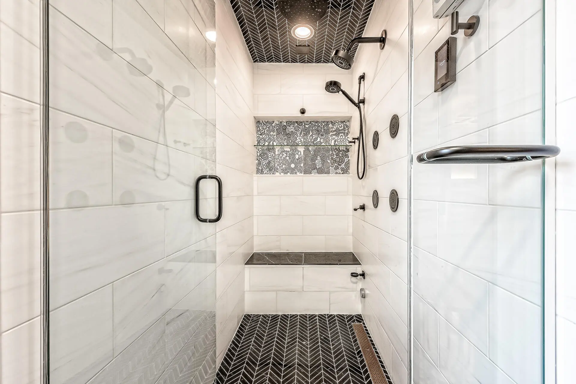 Design First Builders Park Ridge luxury shower with black chevron tile ceiling and floor, white marble walls, multiple body sprays, and built-in bench