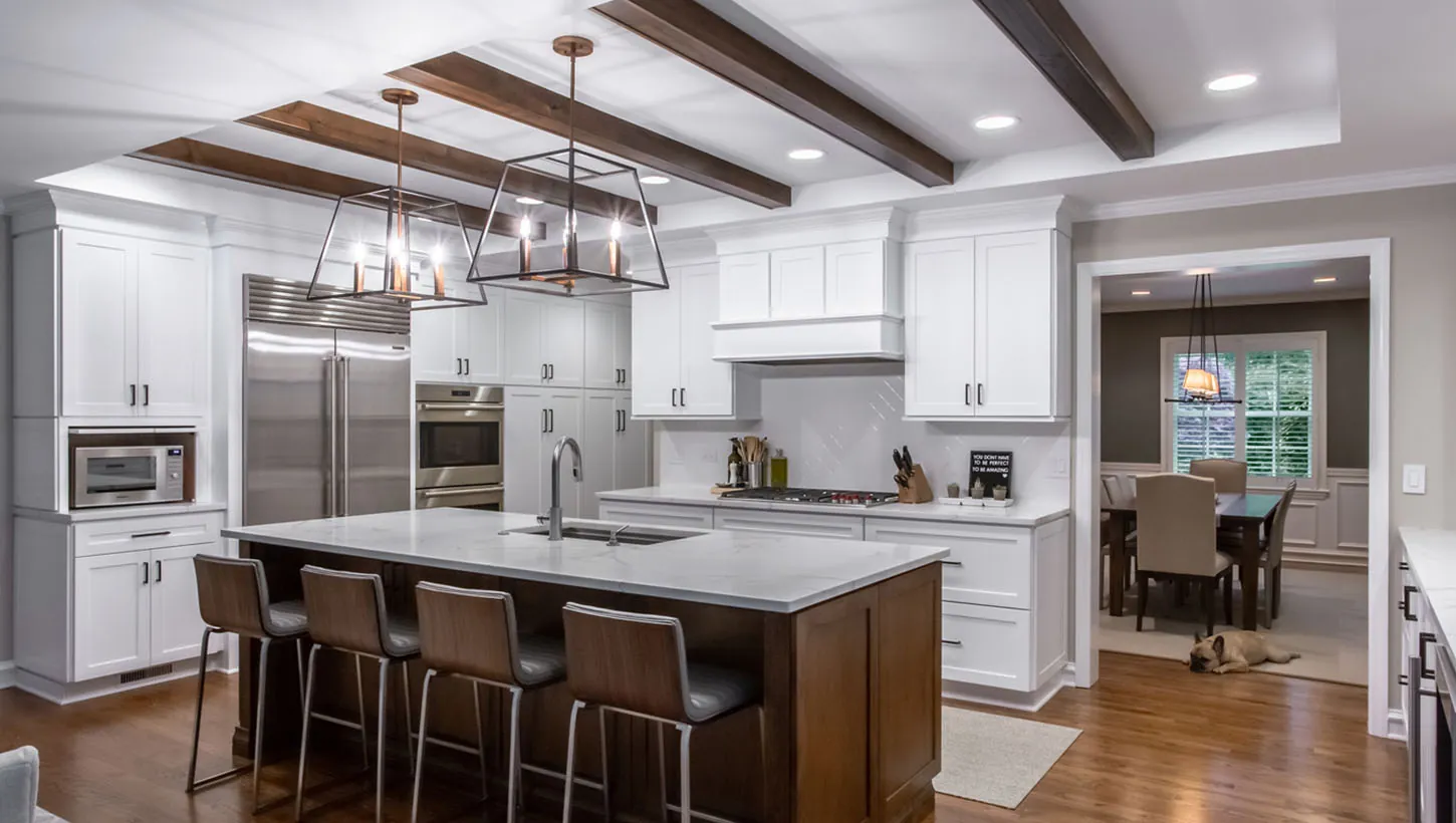 Modern kitchen renovation with exposed wood ceiling beams, two-tone cabinets, large island with seating, and open concept layout by Design First Builders in Highland Park