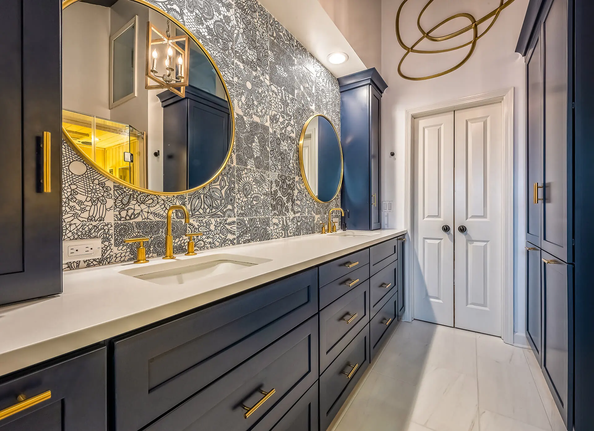 Design First Builders Park Ridge luxury bathroom with navy blue cabinets, brass fixtures, round mirrors, dramatic wallpaper, and white quartz countertops