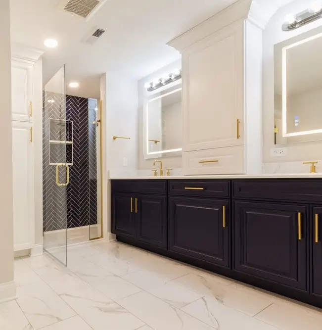 Luxury master bathroom renovation by Design First Builders featuring navy double vanity, gold fixtures, herringbone tile shower, marble flooring, and white upper cabinets in Illinois