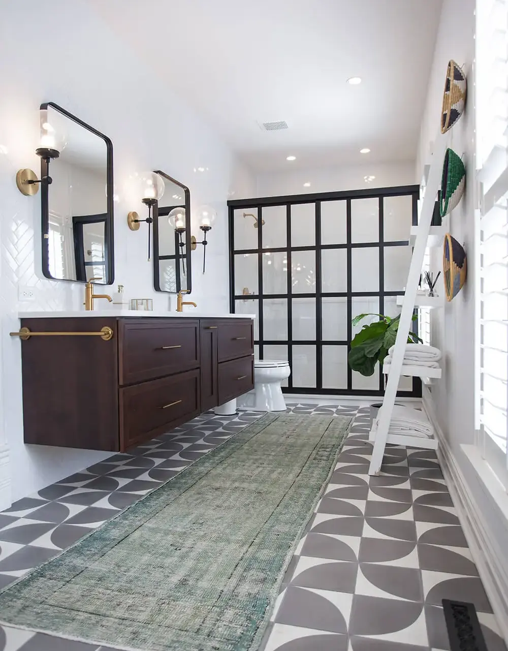 Modern bathroom with geometric patterned floor tiles, dark wood floating vanity with dual sinks, black grid shower enclosure, and brass fixtures