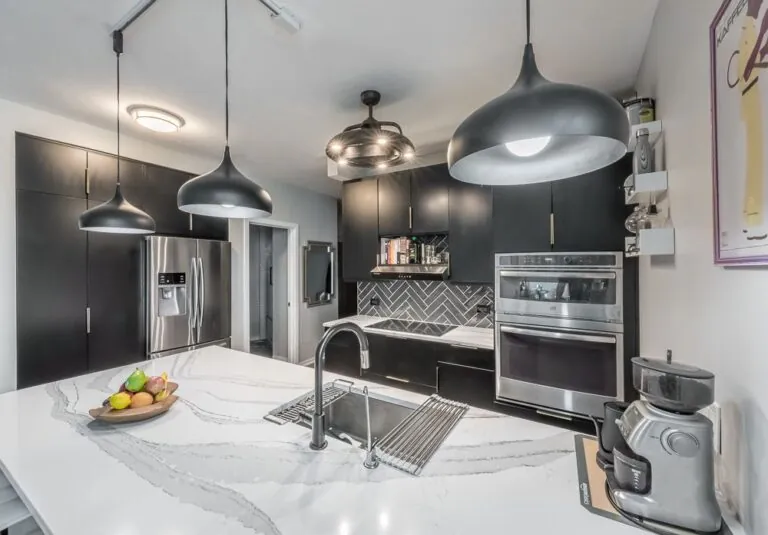 Modern black kitchen remodel with quartz countertops, pendant lighting, and herringbone backsplash by Design First Builders