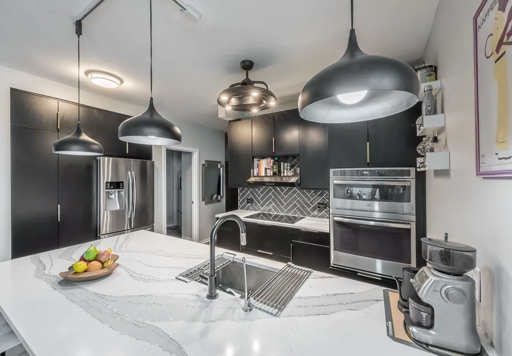 Modern black kitchen remodel with quartz countertops, pendant lighting, and herringbone backsplash by Design First Builders