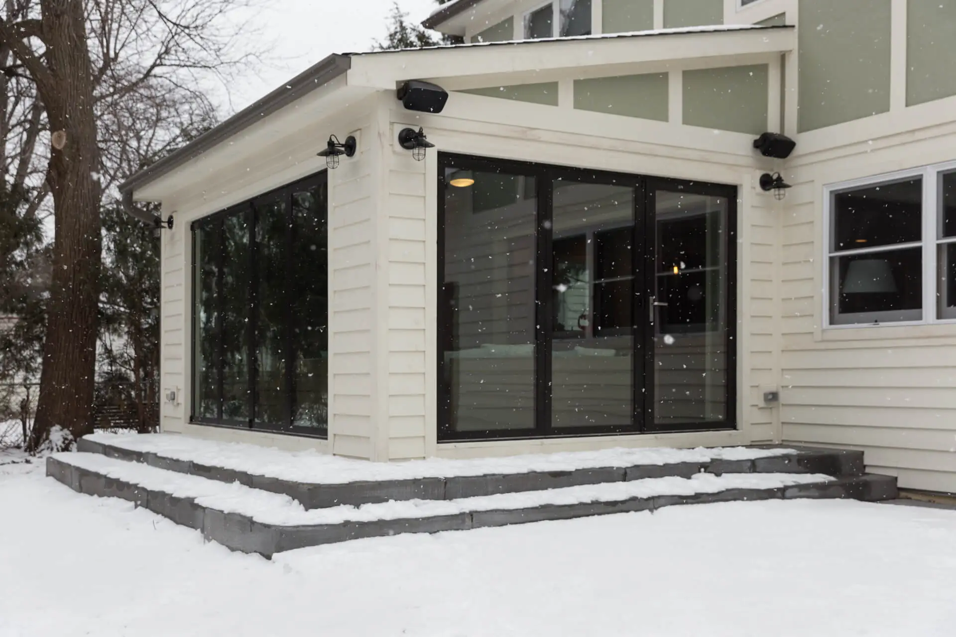 Modern sunroom addition with black-framed sliding doors in Naperville, Illinois during winter snowfall