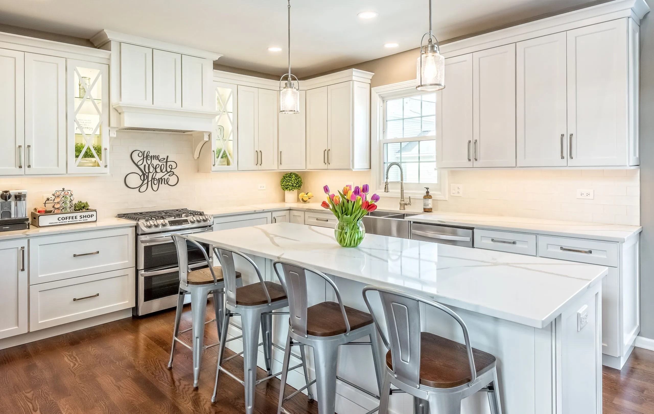 Modern white kitchen with large island, pendant lighting, and stainless steel appliances by Design First Builders